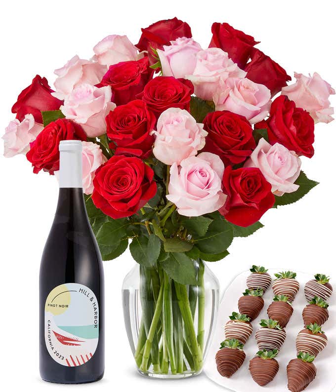 A mixed bouquet of 2 dozen red and blush roses in a clear vase is paired with a bottle of Hill & Harbor Pinot Noir and 12 chocolate-covered strawberries.
