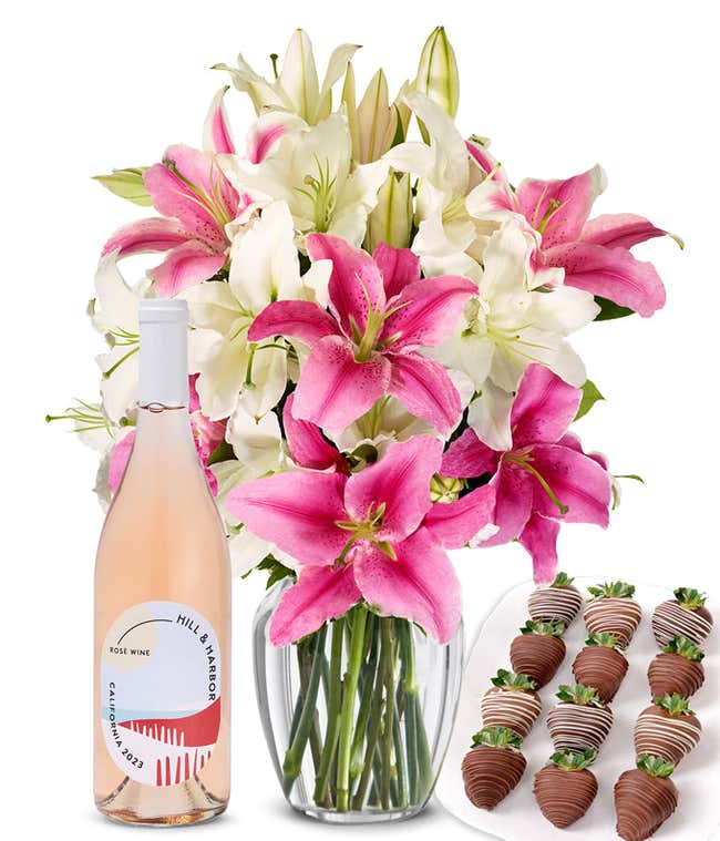 A bouquet of pink and white lilies arranged in a clear glass vase is paired with a bottle of Hill &amp; Harbor Ros&eacute; and 12 chocolate-covered strawberries.
